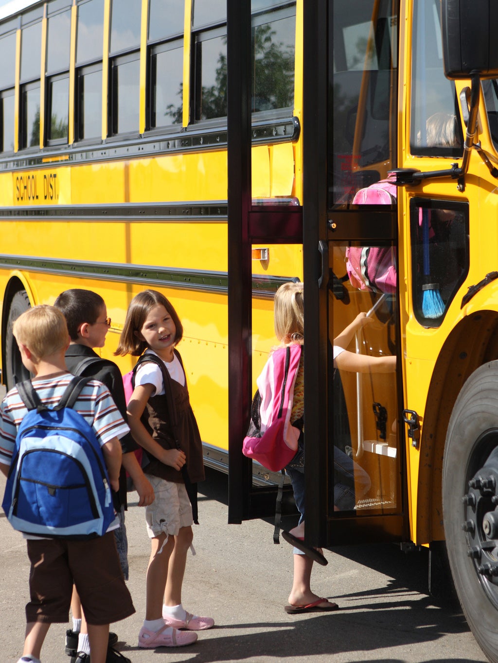 Young children stand in a line, waiting to get onto a yellow school bus.