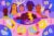 Hand-drawn illustration: Six women of various skin colors, ethnicities, and dress look at the viewer. Bloody, substitute sanitary items are below: newspaper, toilet paper, rags and notepaper. In the corners of the illustration are menstrual cups, pads, and tampons with “$$$” price tags. Inset: A female figure lies on a bed, holding a hot water bottle with a stack of books, notepaper, and a backpack surrounding her. She looks at a clock with a worried look on her face.